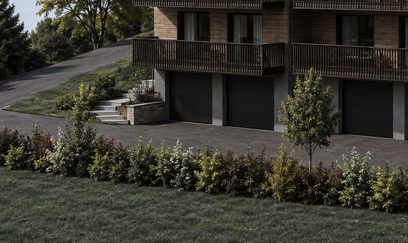 Les abords au niveau du rez : les portes de garage sombres, la rampe d'accès, les escaliers de pierre et les massifs plantés qui bordent le parvis.